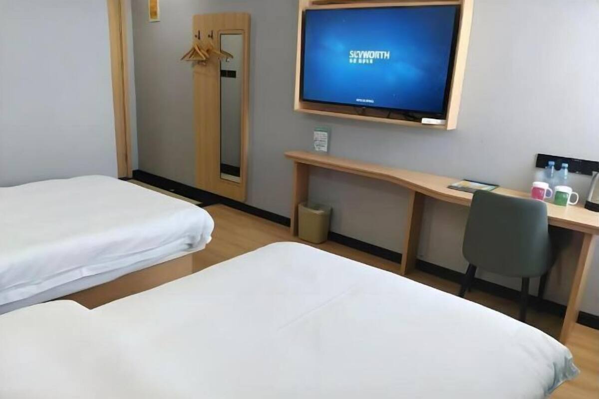 Habitación de hotel con dos camas individuales, un escritorio con silla, televisión y espejo.
