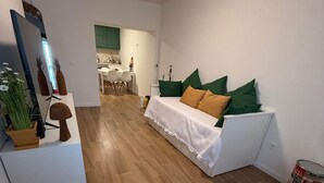 A modern living room with a sofa, a dining area, and a kitchen in the background.