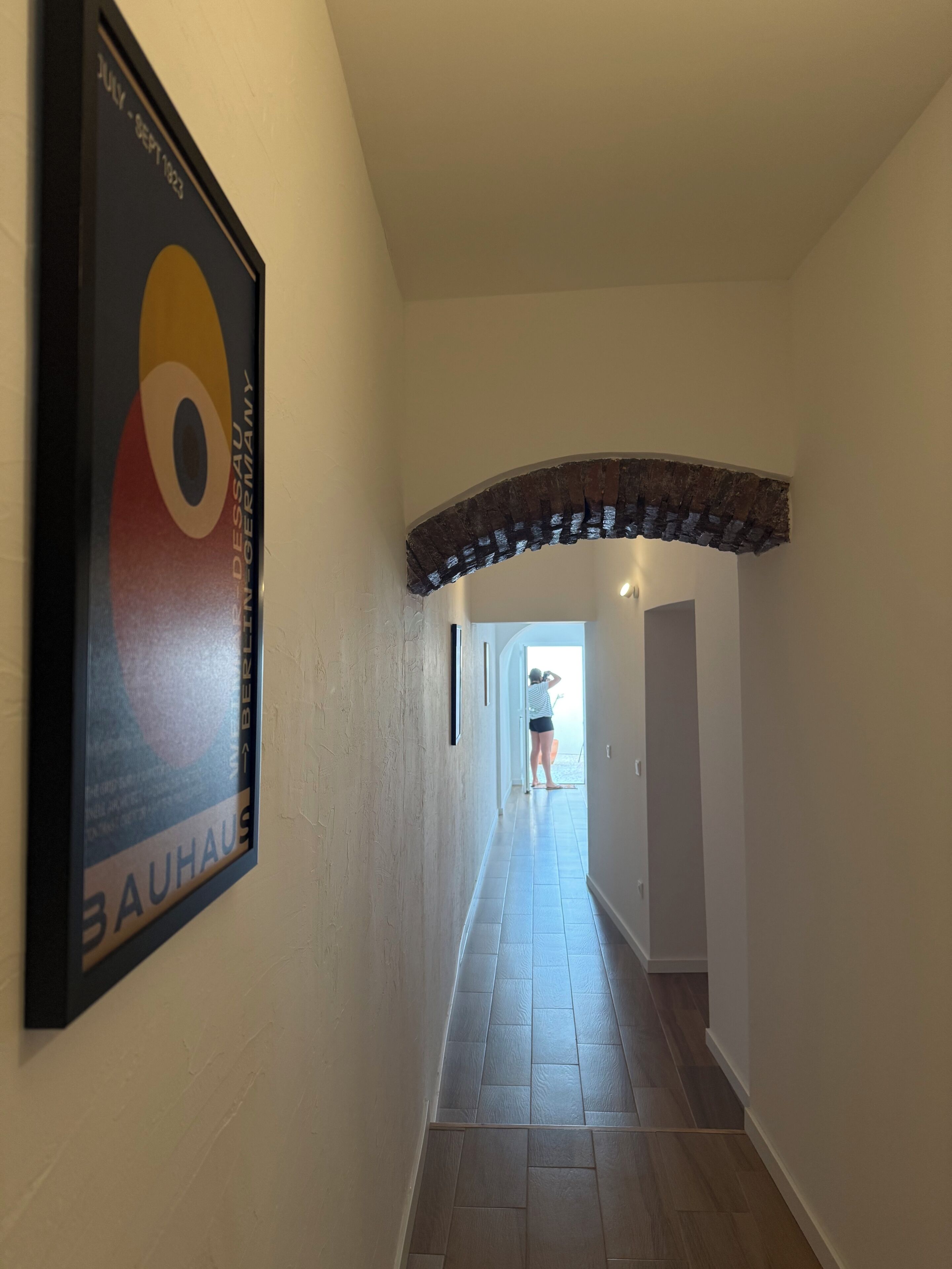 Een gang met een lijst op de muur, een betegelde vloer en een gewelfde doorgang naar een andere kamer.