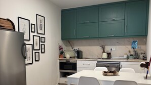 A modern kitchen with teal cabinets, a white dining table with two chairs, and a refrigerator.