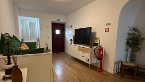 A modern living room with a flat-screen TV, a sofa, and a coffee table. There is a wooden floor and a door in the background.