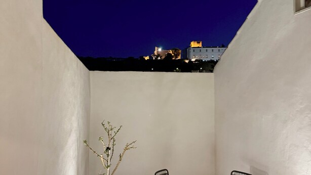 A small outdoor patio with a tiled floor, a potted plant, two chairs, and a table.