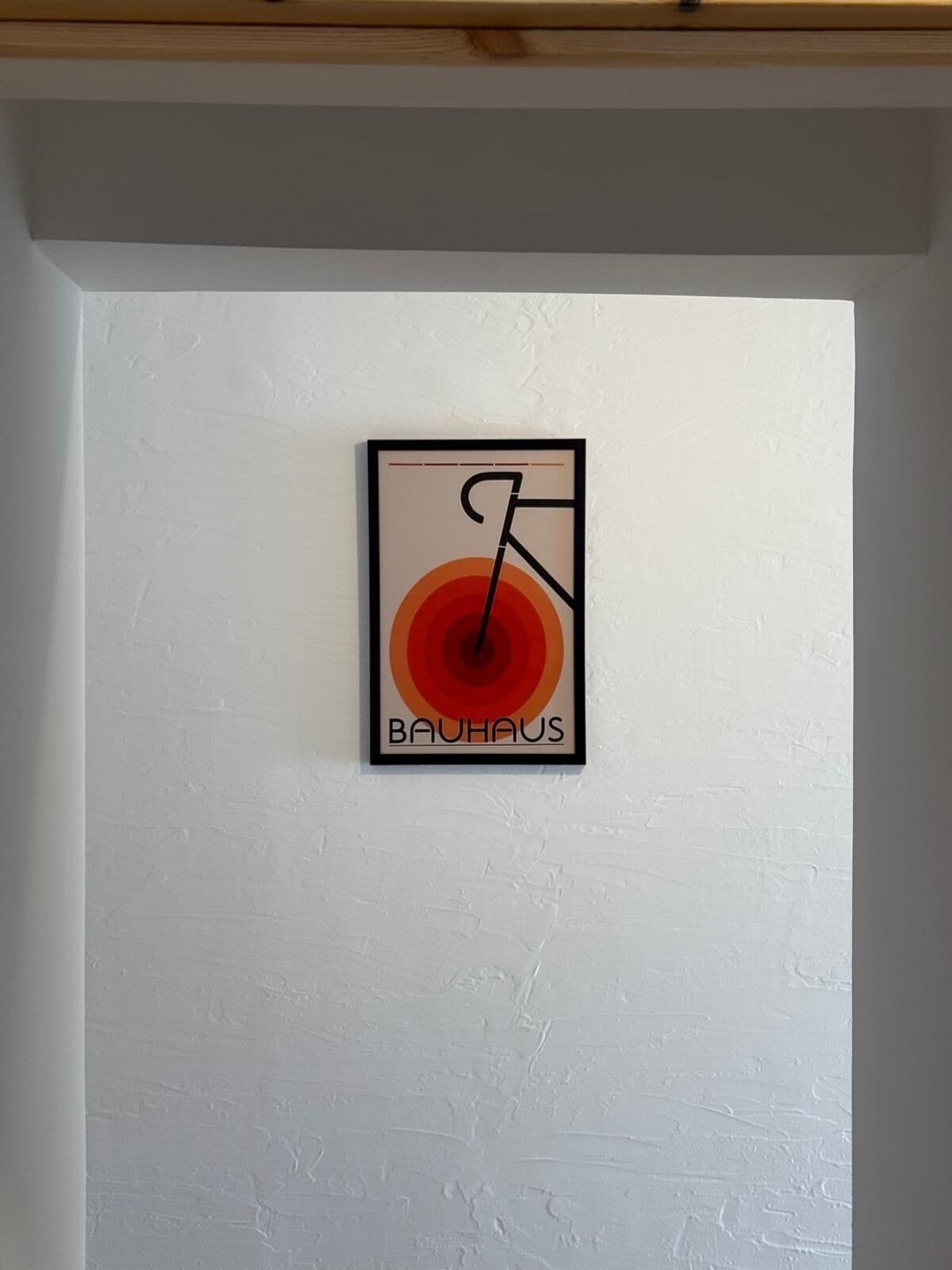 A framed artwork with a bicycle and the word "BAUHAUS" on a white wall.