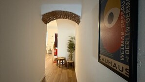 A hallway with a wooden floor, a brick archway, and a framed poster on the wall.