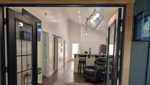A spacious hallway with a large rug, a dining area with chairs, and a kitchen in the background. - The Hawthorne Place (Buena Vista)