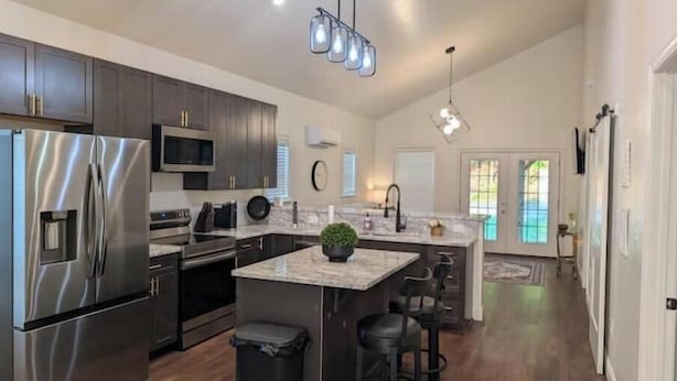 A modern kitchen with stainless steel appliances, dark wood cabinets, and a central island with bar stools. - The Hawthorne Place (Buena Vista)