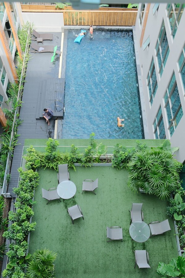 A rooftop pool with clear blue water, surrounded by green artificial grass and outdoor furniture.