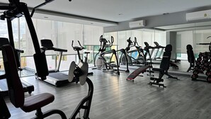 Un gimnasio con diversos equipos de ejercicio, amplias ventanas y piso de madera.