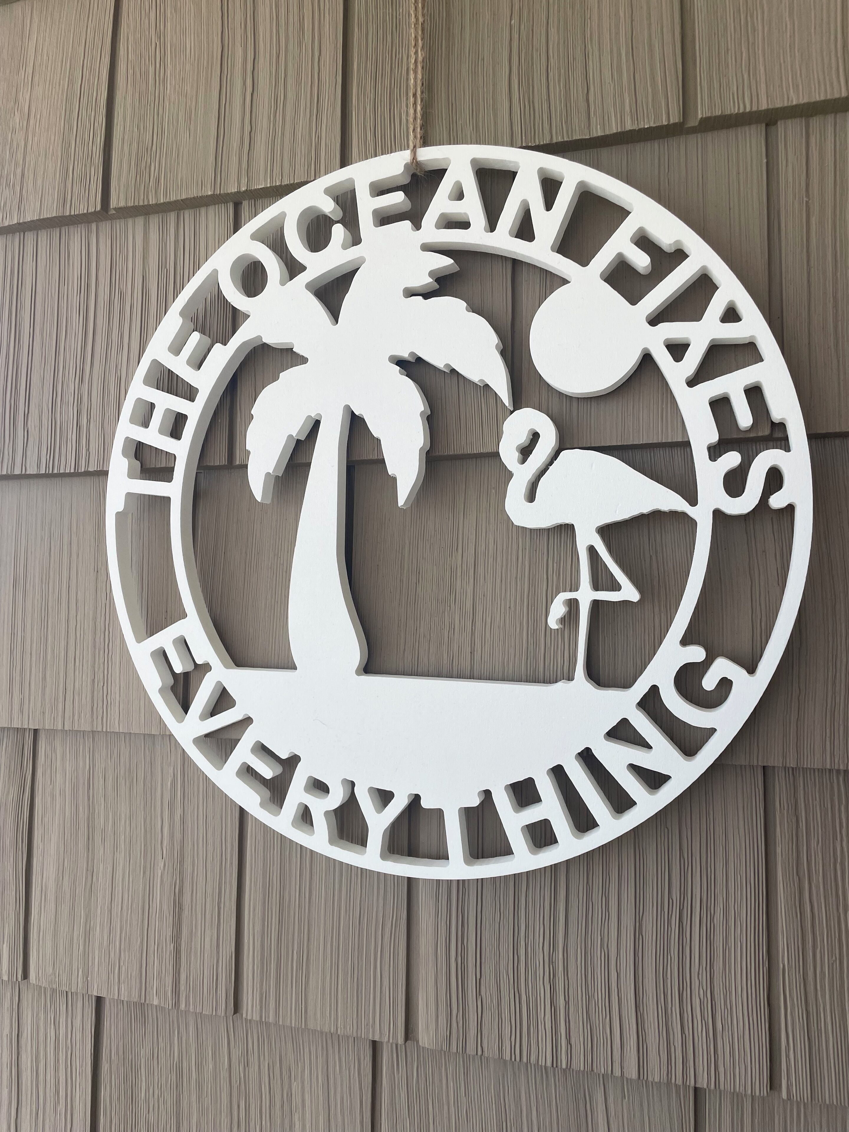 A circular sign with the text "THE OCEAN FIXES EVERYTHING" and silhouettes of a palm tree, a flamingo, and a fish.
