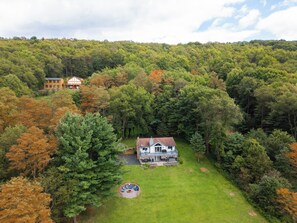 A large house surrounded by a dense forest with a well-maintained lawn and outdoor seating area.