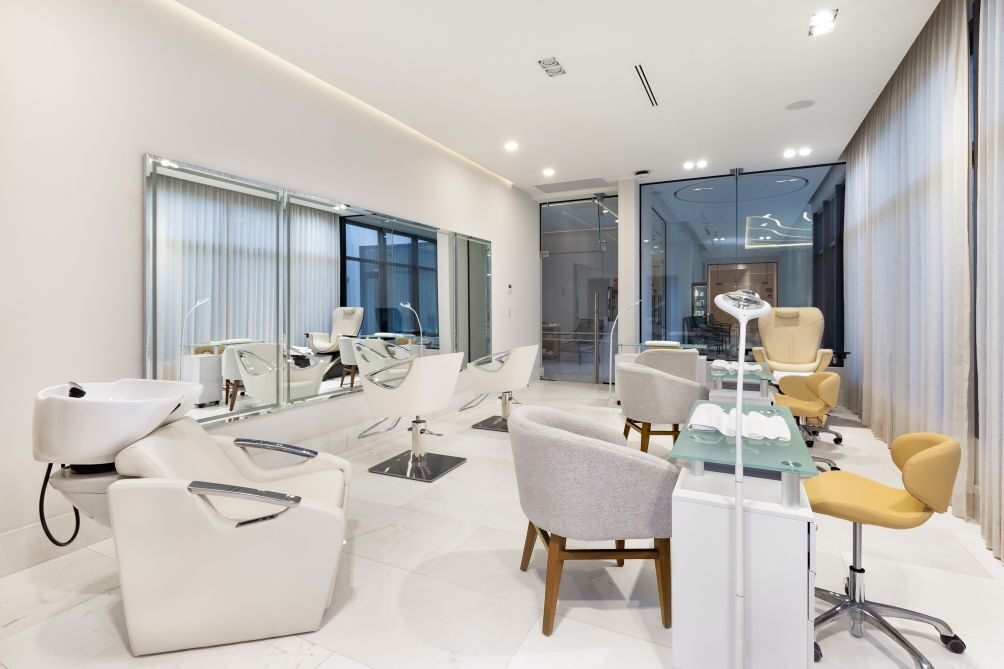 A modern, well-lit room with a large mirror, white chairs, and a glass table.