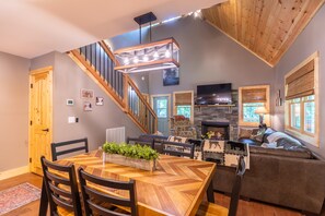 Un interior moderno con comedor, chimenea, escalera y sala de estar con sofá y televisión.