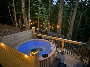 A hot tub on a wooden deck surrounded by trees, with string lights.