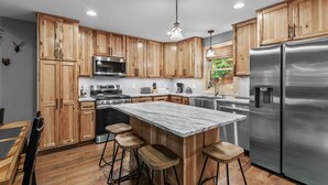 A modern kitchen with wooden cabinets, stainless steel appliances, and a marble island with bar stools. - Bear Necessities - Hot tub, Pet Friendly, Games, Fire table, Beech Mtn (Beech Mountain)