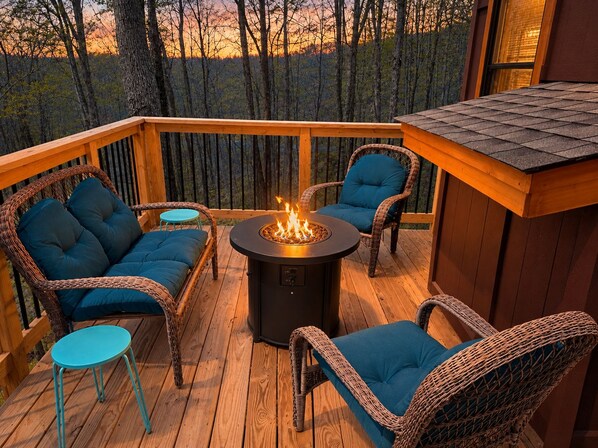 Una terraza con mobiliario de mimbre, un hogar central y vistas al bosque.