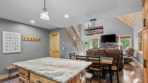 A spacious living area with a dining table, sofa, and a kitchen area with a marble countertop. - Bear Necessities - Hot tub, Pet Friendly, Games, Fire table, Beech Mtn (Beech Mountain)