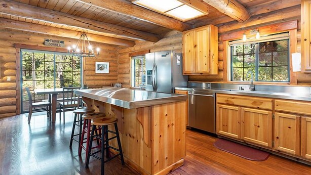 A log cabin kitchen with wooden cabinets, a stainless steel refrigerator, and a bar area with stools.