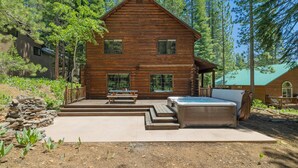 A wooden cabin with a hot tub, a patio, and a stone wall.