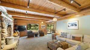 A cozy log cabin interior with a stone fireplace, a stone wall, a large window, a sofa, and a television.