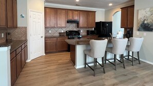 Een moderne keuken met houten kastjes, een zwarte koelkast en een centraal eiland met barstoelen.