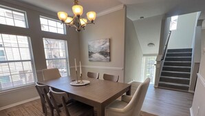 Een eetruimte met een houten tafel, zes stoelen, een kroonluchter en een schilderij aan de muur.