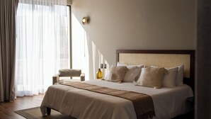 Ein modernes Hotelzimmer mit einem großen Bett, Holzboden und einem großen Fenster mit leichtem Vorhang.