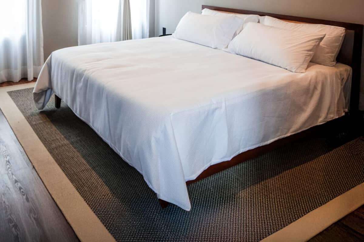 Una cama bien hecha en una habitación con un ventanal grande, una lámpara de pared y una viga de techo de madera.