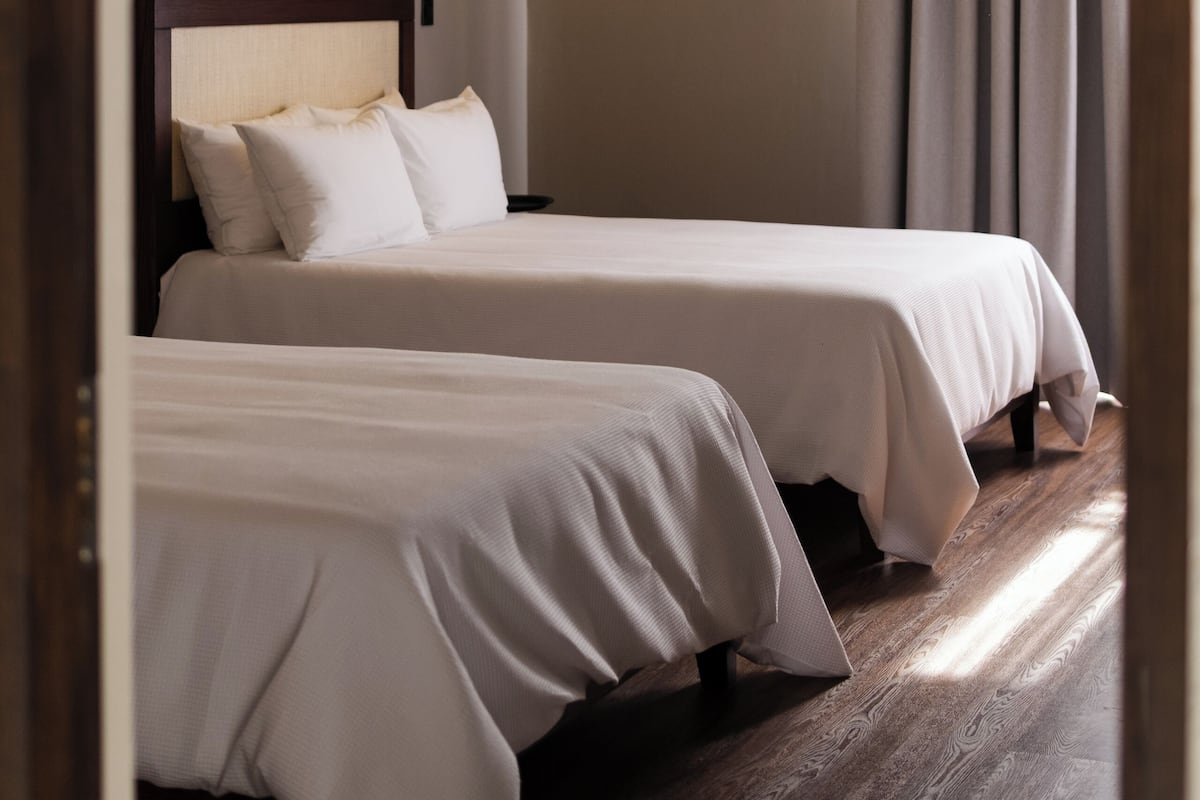 Habitación de hotel con dos camas, una lámpara en el techo y vistas al exterior a través de una ventana con cortinas.