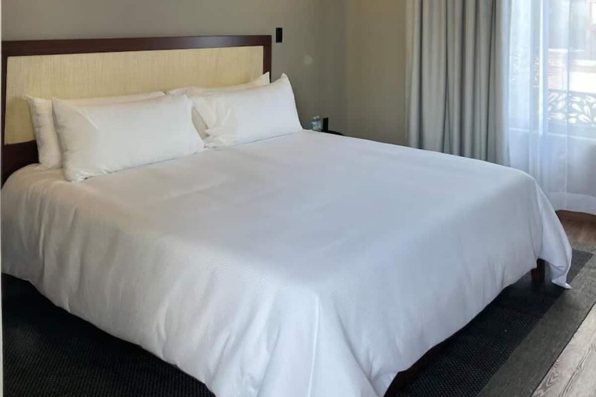 Habitación de hotel con una cama grande, cabecero, luz empotrada en la pared y ventana con cortinas.