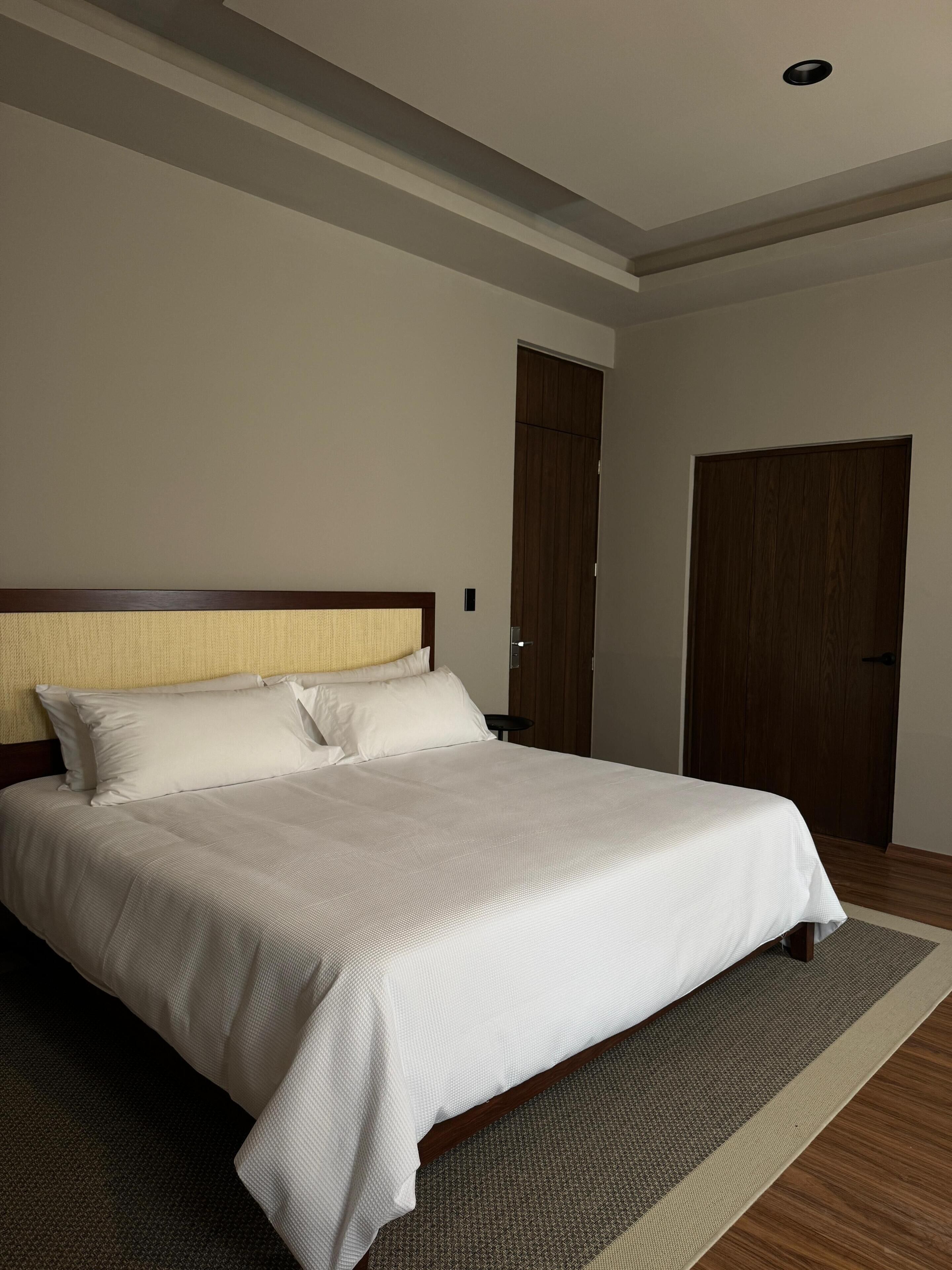 A neatly made bed with a wooden headboard and white bedding in a room with a wooden floor and a large wardrobe.