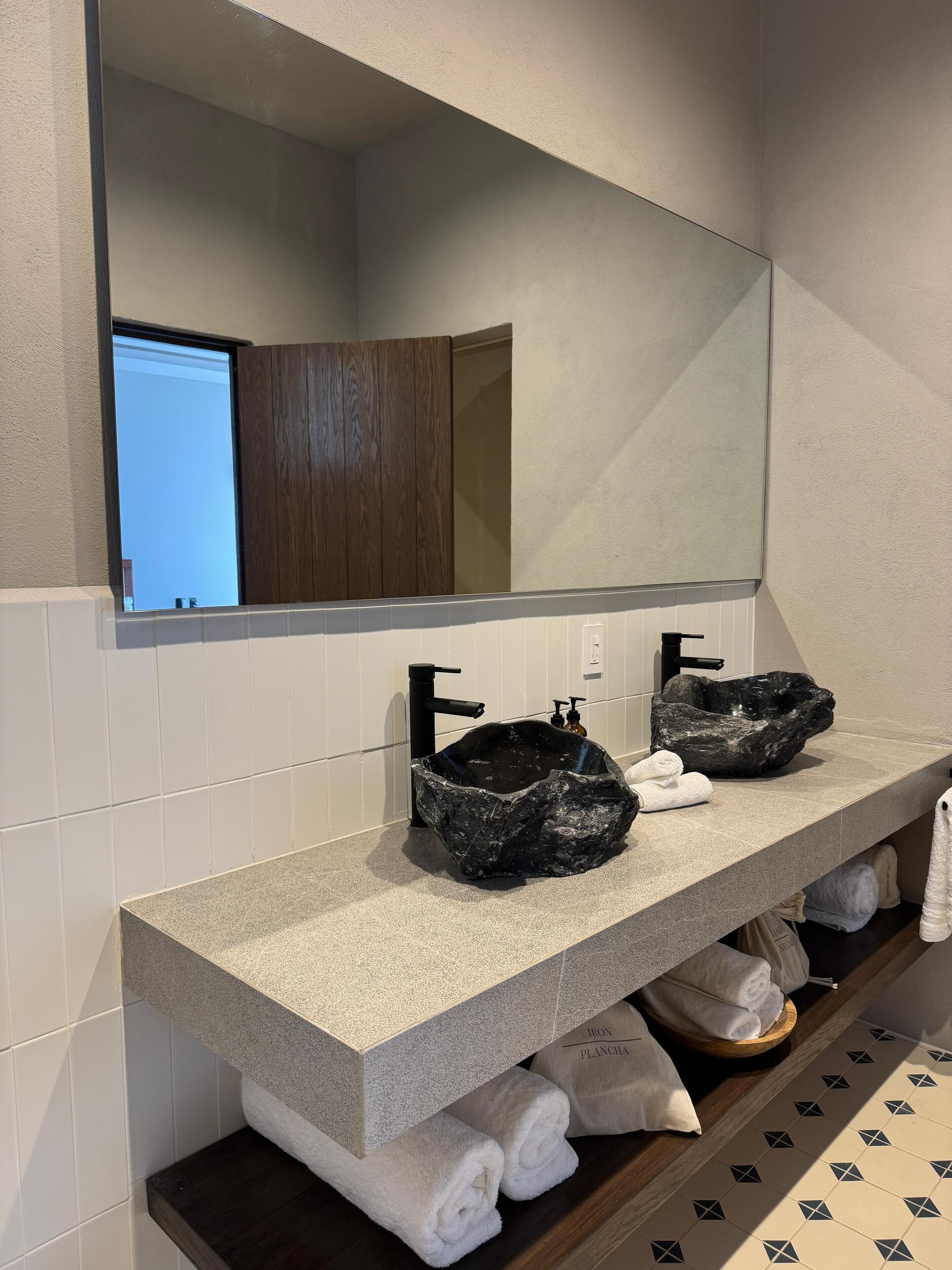 A bathroom with a granite countertop, two black vessel sinks, a large mirror, and a wooden cabinet.