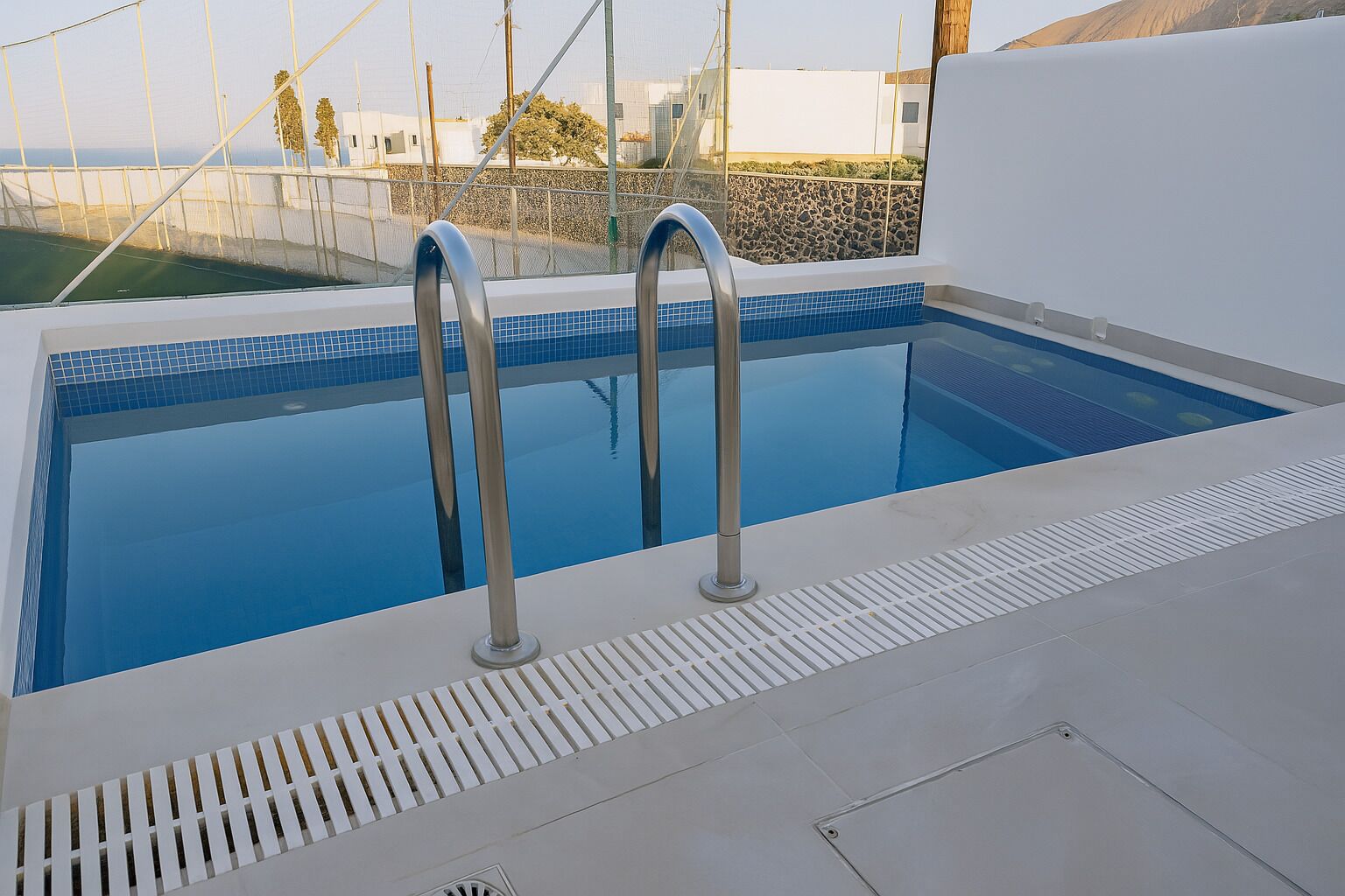 A modern indoor swimming pool with two metal ladders, clear blue water, and a tiled edge.