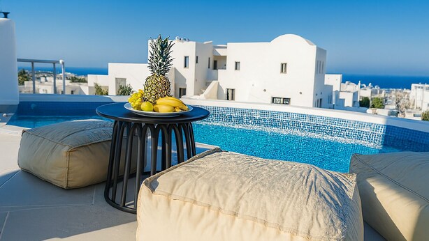 Un espace piscine aménagé sur le toit, avec une table et des coussins, ainsi qu’un ananas et des bananes posés sur la table.