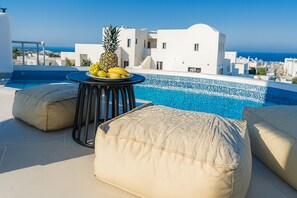 Un espace piscine aménagé sur le toit, avec une table et des coussins, ainsi qu’un ananas et des bananes posés sur la table.
