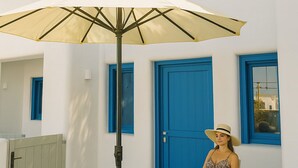 Une femme est assise sous un grand parasol, devant un bâtiment blanc agrémenté de touches de bleu.