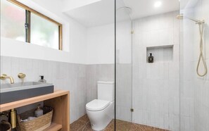 A modern bathroom with a glass-enclosed shower, a sink with gold fixtures, and a toilet.