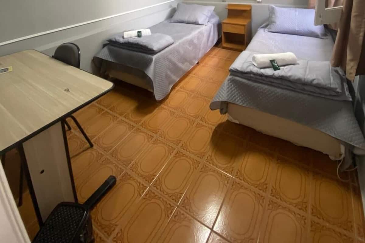 Une petite pièce, de taille modeste, comprenant deux lits simples, un bureau et une chaise.