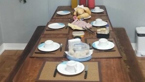 Una mesa de comedor lista para una comida, con platos, vasos y cubiertos. Un televisor está montado en la pared sobre la mesa.