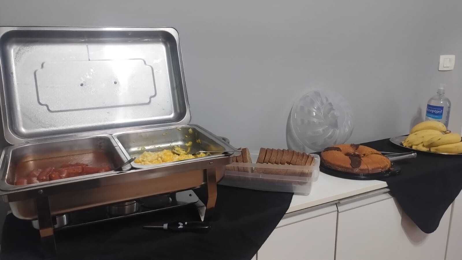 Montaje tipo buffet con diversas opciones de comida, incluyendo huevos revueltos, salchichas y un pastel de chocolate.