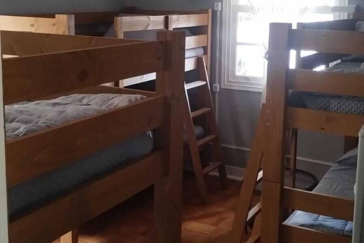 Une chambre de dortoir avec des lits superposés, une fenêtre avec des rideaux légers et un plancher en bois.