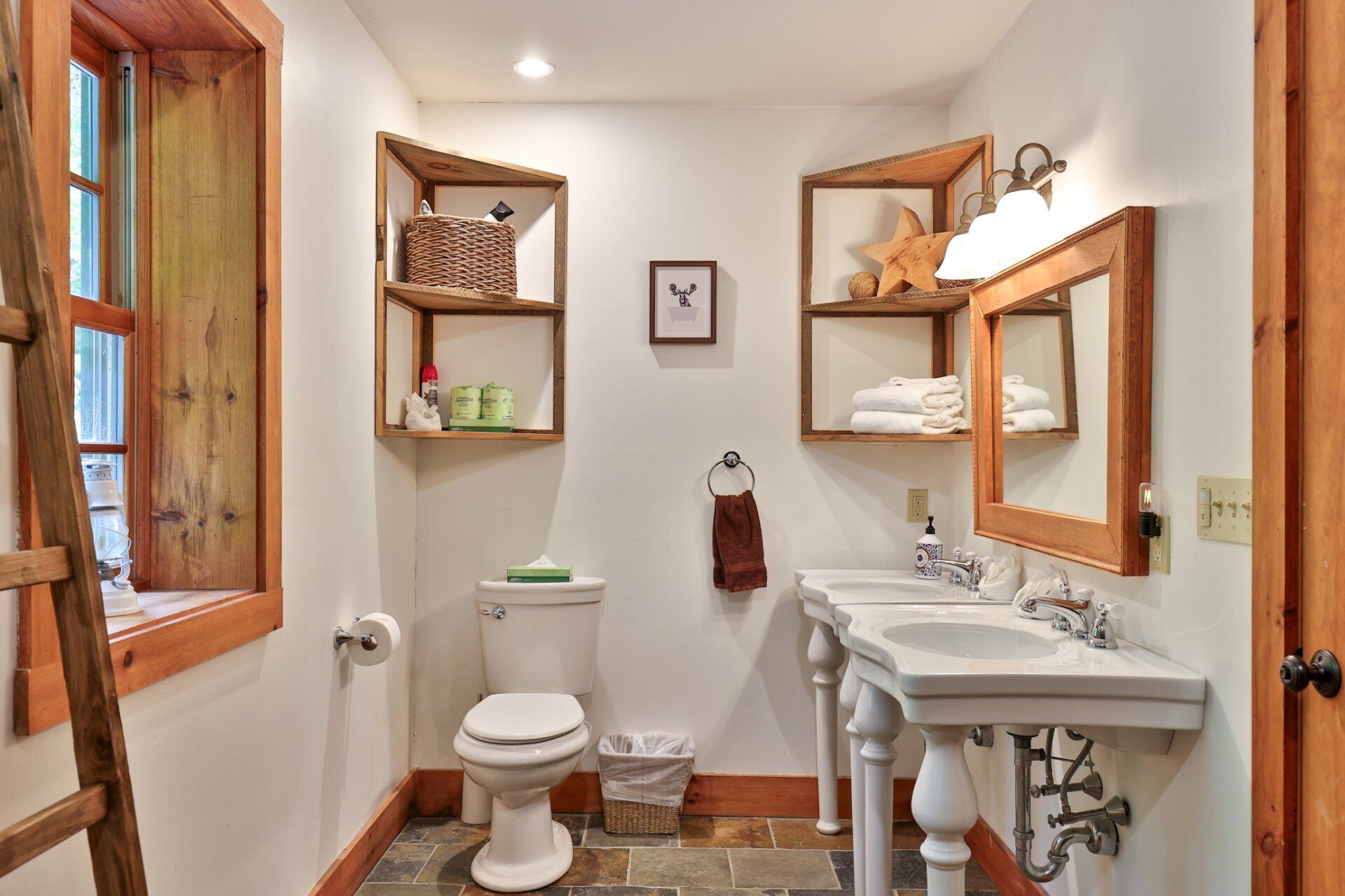 A bathroom with a toilet, two sinks, wooden shelves, a framed mirror, and a star decoration.