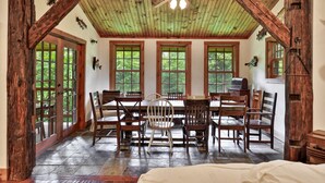 A rustic dining room with a wooden ceiling, large windows, and a central table with chairs.