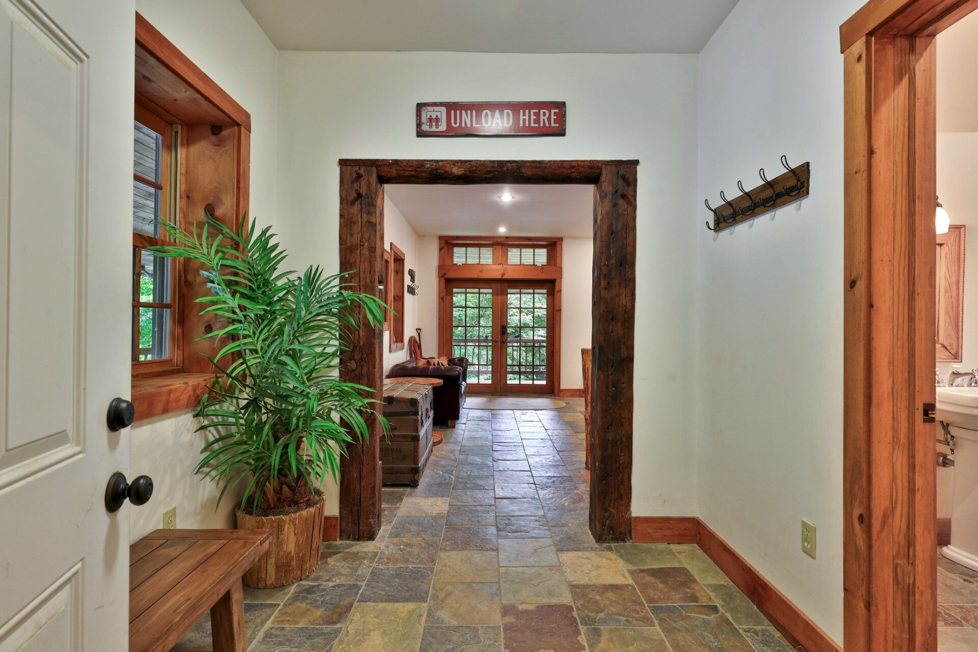 A hallway with a wooden door, a potted plant, a sign that reads "UNLOAD HERE", and a coat rack.