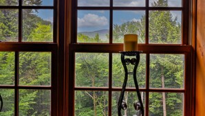 A window with a candle holder and a view of a forested landscape.