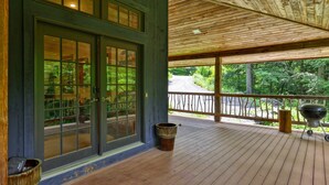 A covered porch with a wooden deck, a grill, and a trash can.