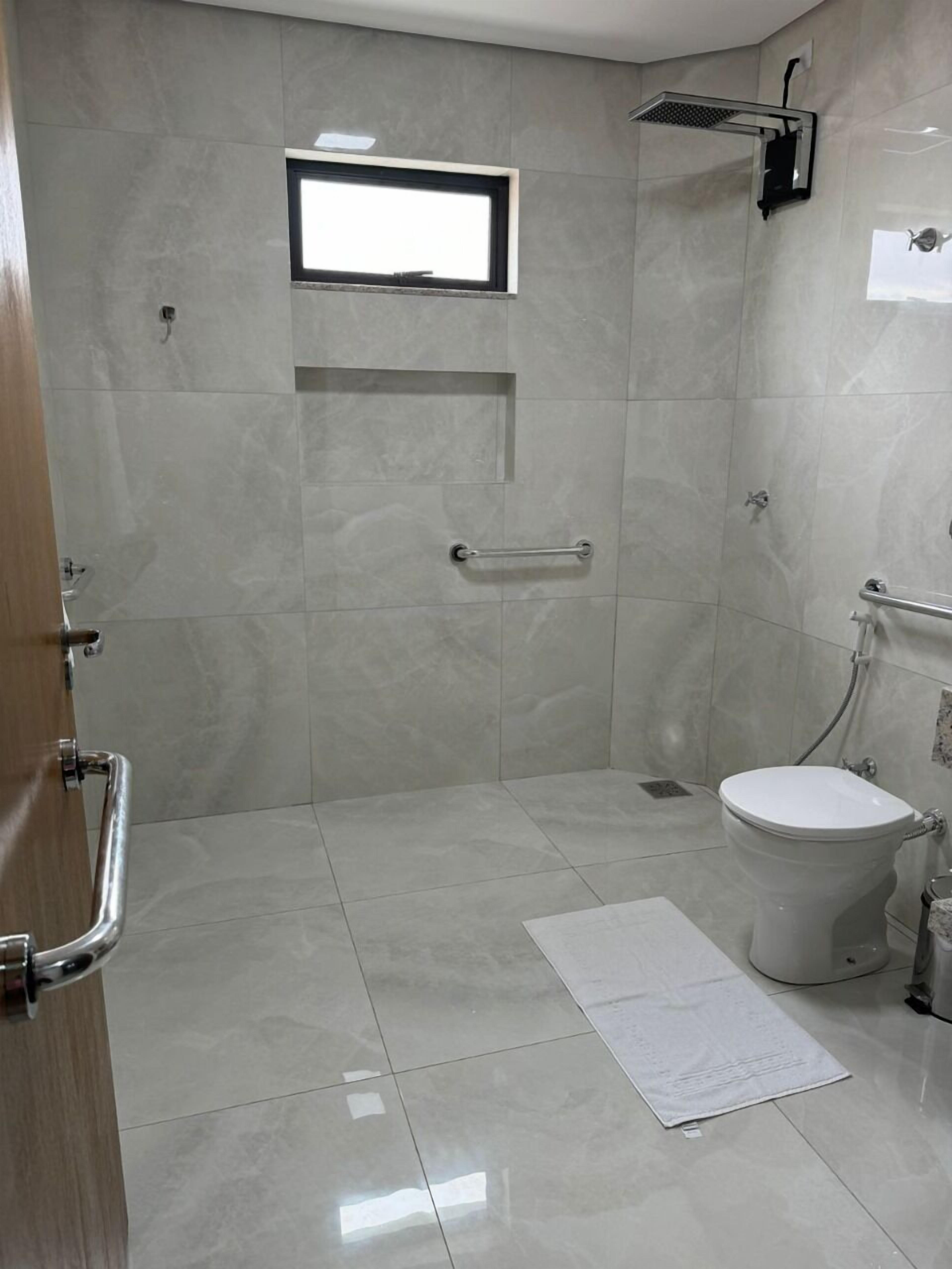A modern bathroom with a walk-in shower, a toilet, and a small window.