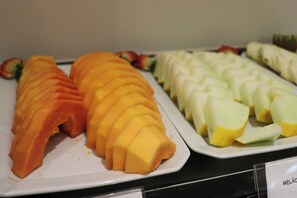 Un buffet con fette di mango e melone disposti su piatti bianchi.