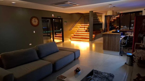 A modern living room with a grey sofa, a coffee table, and a staircase with illuminated steps leading to an upper level. - Hotel Garden (Jardim)