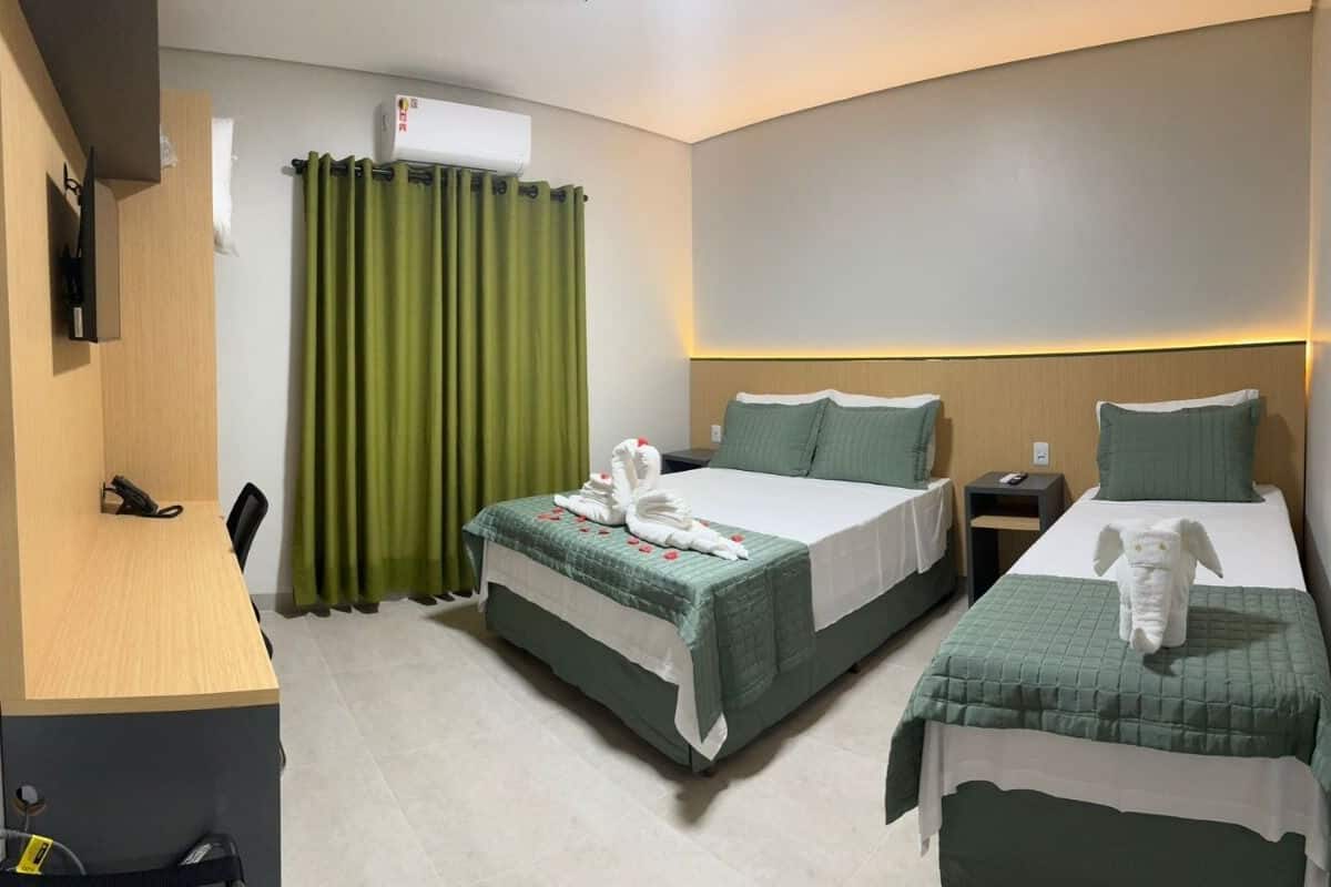 A hotel room with two beds, a desk, a chair, a small table, and a green curtain.