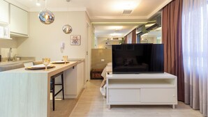 Uma sala de estar moderna com televisão, área de jantar com mesa e cadeiras, e cozinha com bancada e armários.